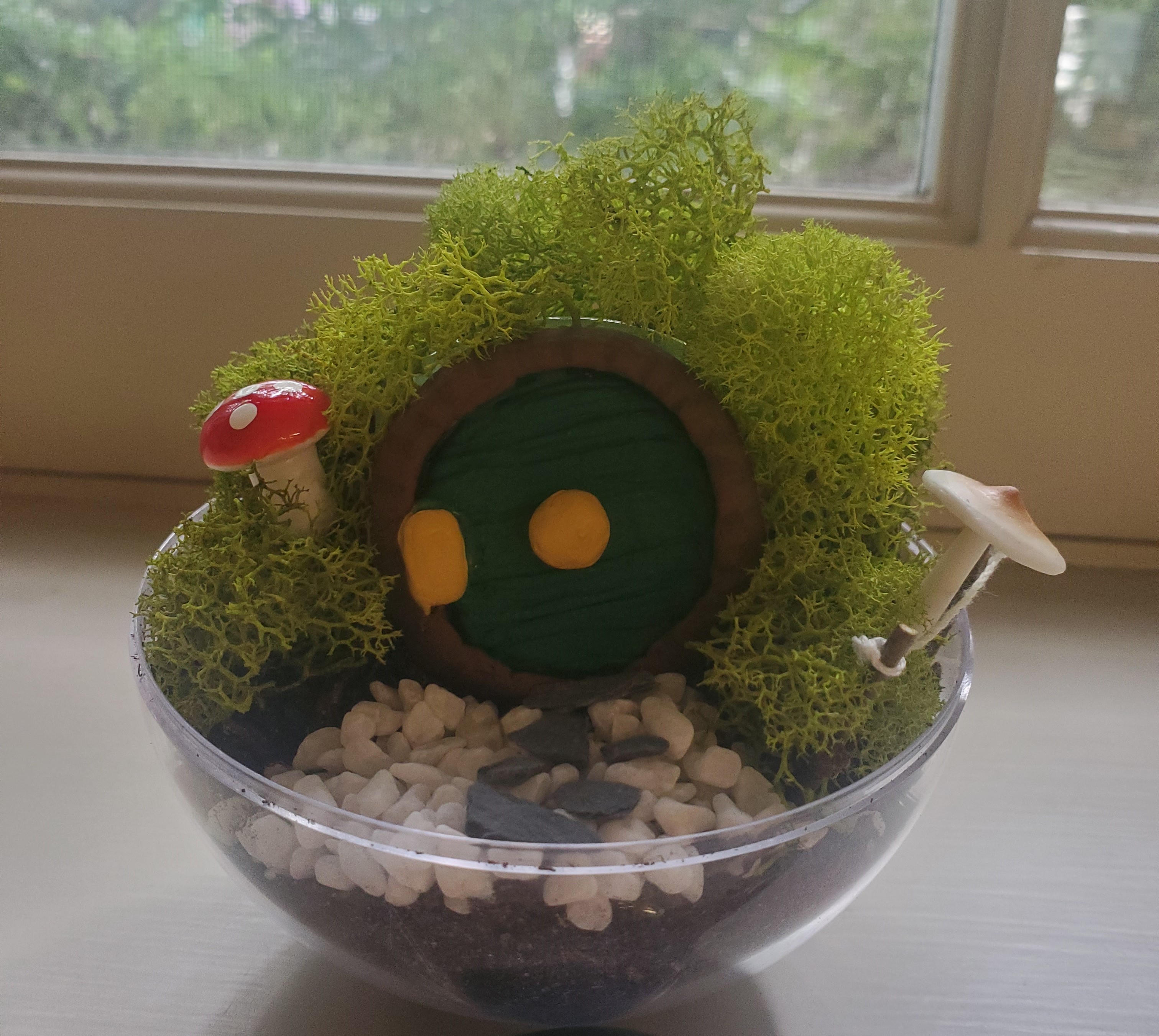 A round terrarium, with a gravel walkway leading up to a round, green hobbit door. 