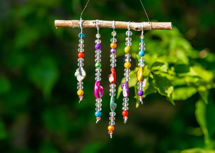 Image of suncatcher made with natural wood and various glass beads against foliage background