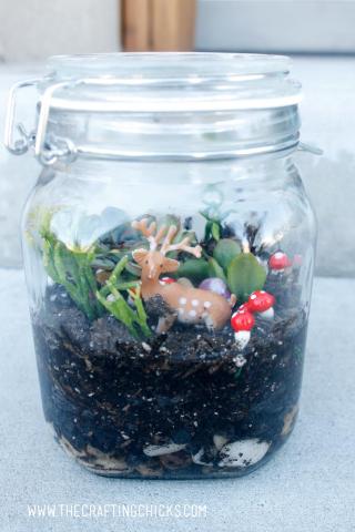 Glass jar terrarium with green plant life, and deer and mushrooms